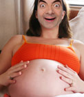 Fotomontaje en el que poner una cara a esta embarazada que se toca la barriga. Aparece recostada en una cama con top y pantalones color 