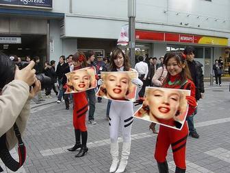 Fotomontaje en el que tres chicas asiáticas sujetan carteles con tu fotografía, en plena calle, con gran expectación.
